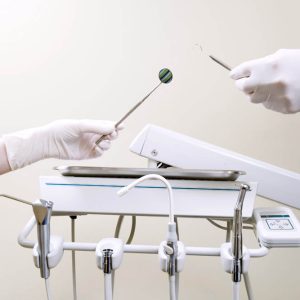 Two people's hands holding exam tools by tray of dental equipment